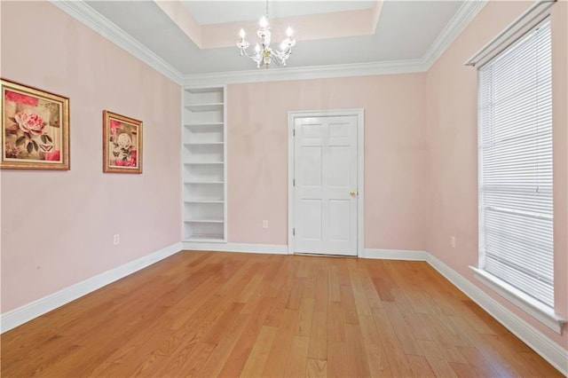 empty room with light wood finished floors, baseboards, a chandelier, built in features, and a raised ceiling