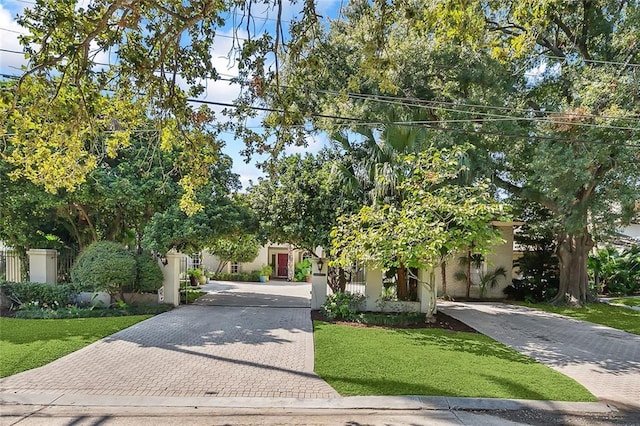 view of property hidden behind natural elements with a front yard, decorative driveway, and fence