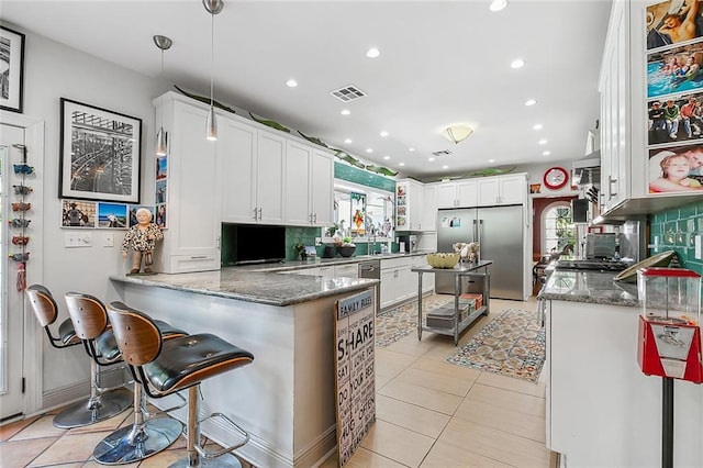 kitchen with visible vents, a peninsula, stone countertops, decorative backsplash, and built in fridge