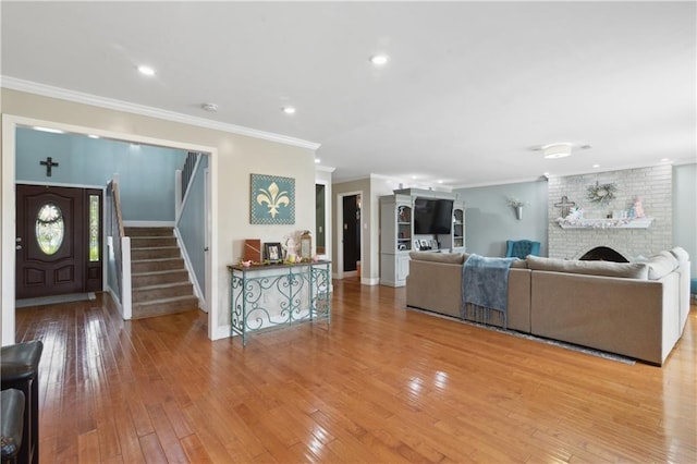 living room featuring baseboards, light wood-type flooring, ornamental molding, a fireplace, and stairway