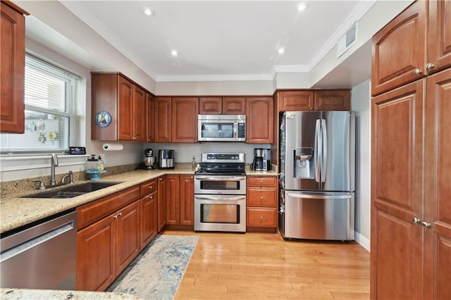 kitchen with light stone counters, light wood finished floors, a sink, appliances with stainless steel finishes, and crown molding