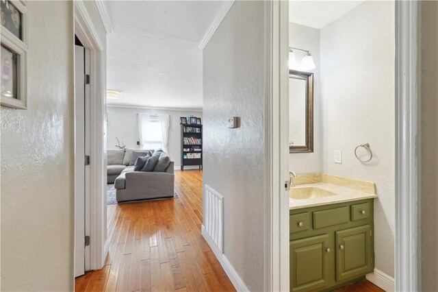 corridor with baseboards, visible vents, light wood finished floors, ornamental molding, and a sink