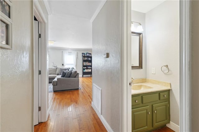 corridor with crown molding, visible vents, a sink, light wood finished floors, and baseboards