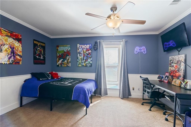 carpeted bedroom with a wainscoted wall, a ceiling fan, visible vents, and ornamental molding