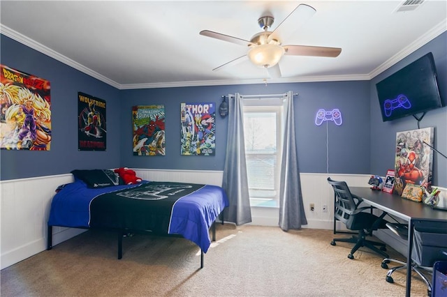 carpeted bedroom featuring visible vents, a ceiling fan, ornamental molding, and a wainscoted wall