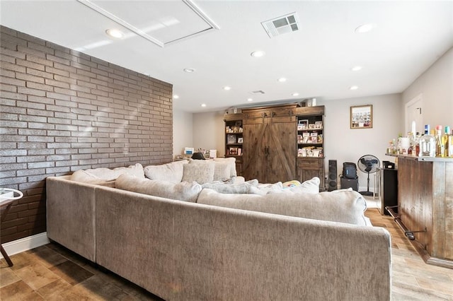 living room with visible vents, wood finished floors, recessed lighting, brick wall, and an accent wall