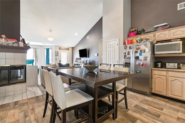 dining room featuring visible vents, high vaulted ceiling, light wood-style flooring, and a tile fireplace