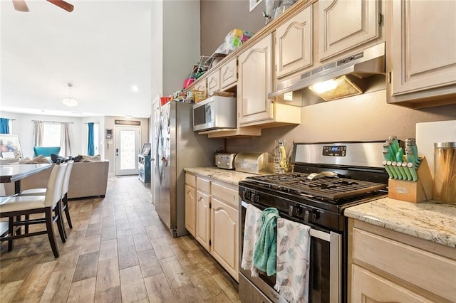 kitchen with light wood-style flooring, under cabinet range hood, light stone counters, open floor plan, and appliances with stainless steel finishes