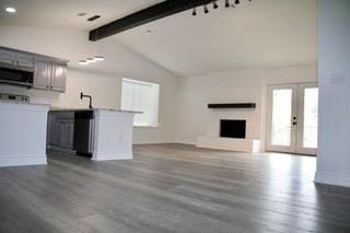 unfurnished living room with dark wood-style floors, french doors, a fireplace, and lofted ceiling with beams