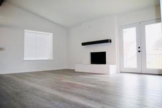 unfurnished living room with french doors, wood finished floors, a fireplace, and vaulted ceiling