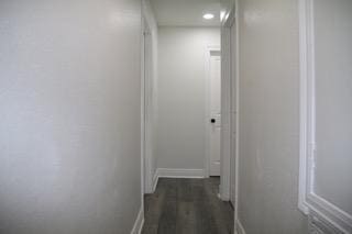 corridor featuring baseboards and dark wood-style floors