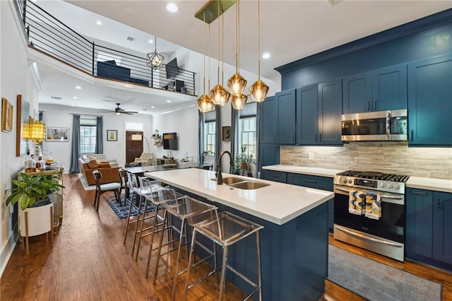 kitchen featuring blue cabinets, an island with sink, a sink, a kitchen breakfast bar, and appliances with stainless steel finishes