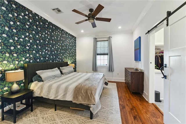 bedroom featuring visible vents, ornamental molding, a barn door, wallpapered walls, and an accent wall