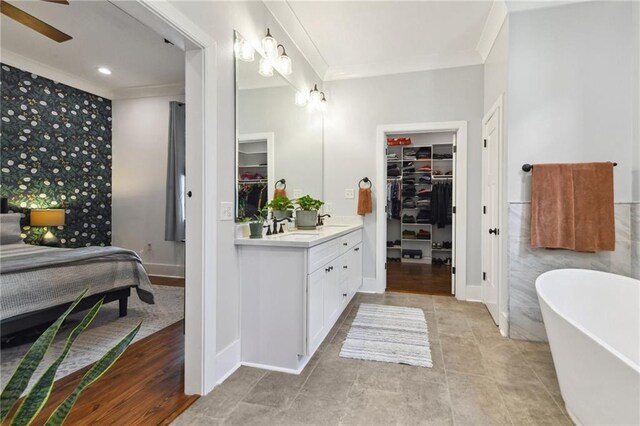 full bath with vanity, a soaking tub, ornamental molding, a walk in closet, and tile walls