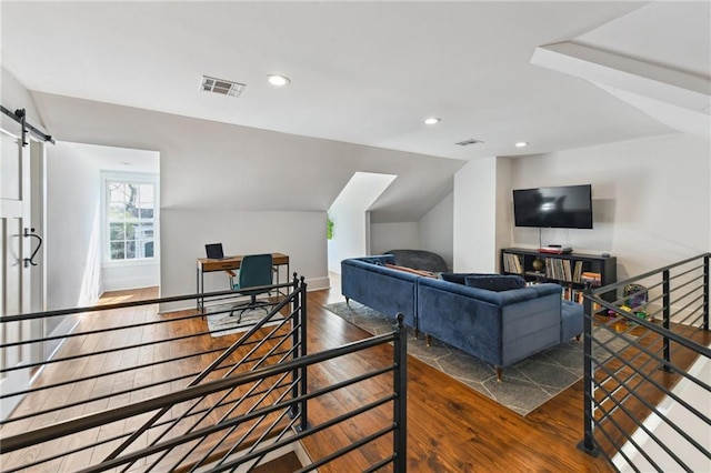 living room with visible vents, recessed lighting, vaulted ceiling, wood-type flooring, and a barn door