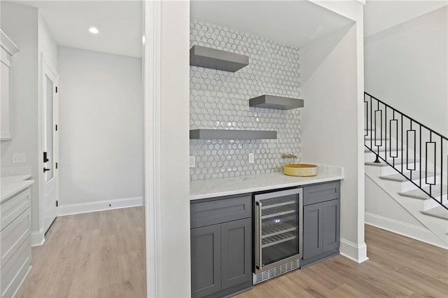 bar featuring decorative backsplash, beverage cooler, baseboards, and light wood finished floors