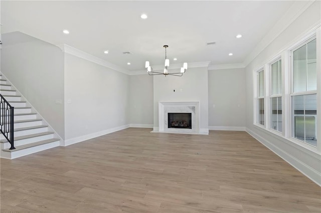 unfurnished living room featuring stairway, light wood-style floors, ornamental molding, and a high end fireplace