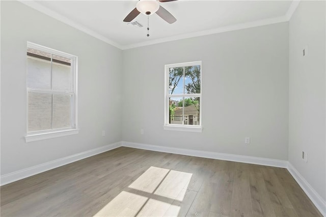 empty room with wood finished floors, crown molding, baseboards, and visible vents