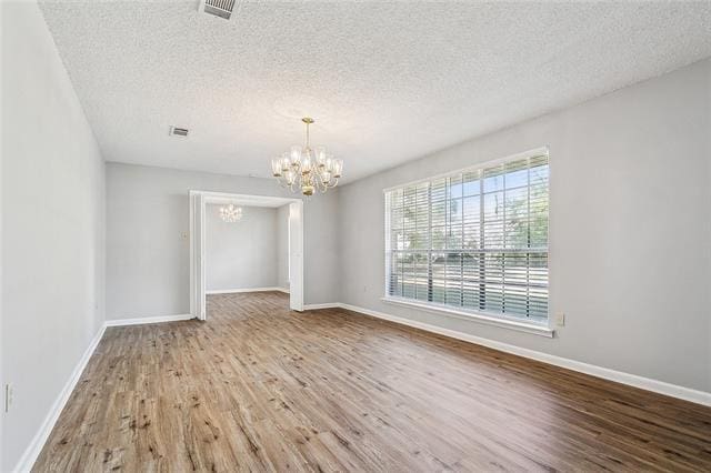 spare room with visible vents, baseboards, an inviting chandelier, and wood finished floors