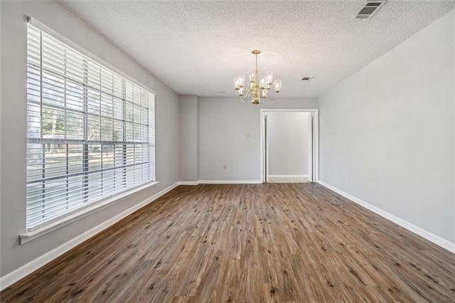 spare room featuring a chandelier, a textured ceiling, baseboards, and wood finished floors