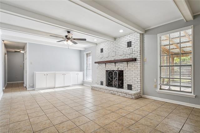 unfurnished living room featuring tile patterned flooring, a brick fireplace, baseboards, beam ceiling, and a ceiling fan