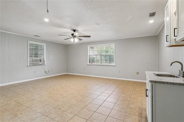 unfurnished living room featuring visible vents, ornamental molding, a sink, a textured ceiling, and ceiling fan