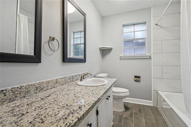 bathroom featuring baseboards, wood tiled floor, toilet, vanity, and a textured ceiling