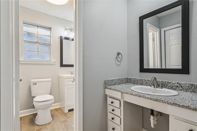 bathroom with baseboards, toilet, wood finished floors, and vanity