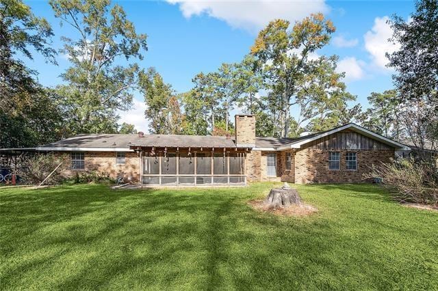 back of property with brick siding, a chimney, a yard, and a sunroom