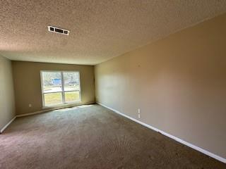 carpeted empty room featuring visible vents, a textured ceiling, and baseboards