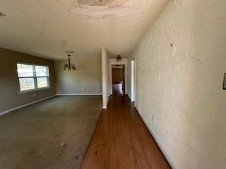 hallway featuring a notable chandelier, a textured ceiling, dark wood-type flooring, and a textured wall