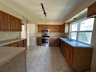 kitchen with stainless steel appliances, a textured ceiling, brown cabinetry, and light countertops