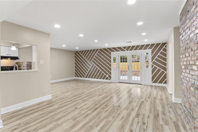 unfurnished living room featuring stairs, light wood-style floors, baseboards, and french doors