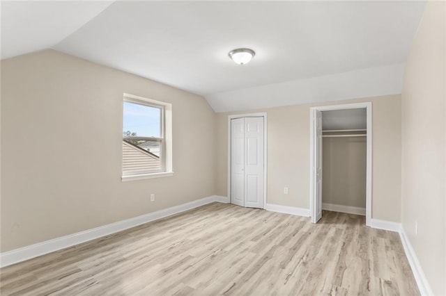 unfurnished bedroom with light wood-type flooring, baseboards, two closets, and vaulted ceiling