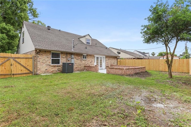 rear view of property with brick siding, roof with shingles, central AC unit, a yard, and a fenced backyard