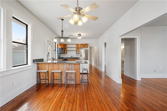 kitchen featuring brown cabinetry, open shelves, a peninsula, appliances with stainless steel finishes, and wood-type flooring