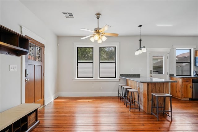 kitchen with a breakfast bar area, brown cabinetry, visible vents, a peninsula, and wood-type flooring