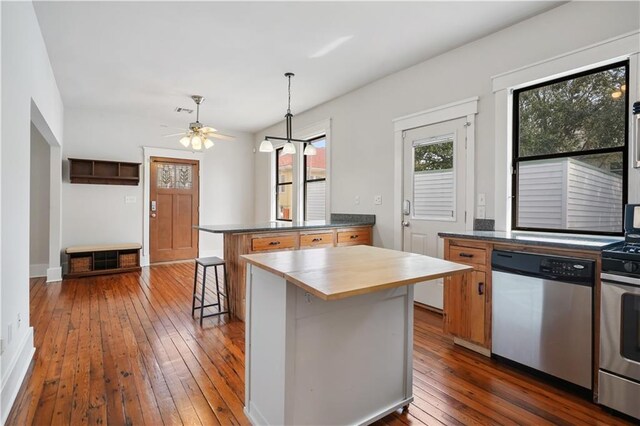 kitchen with a kitchen breakfast bar, dark wood finished floors, a peninsula, appliances with stainless steel finishes, and hanging light fixtures