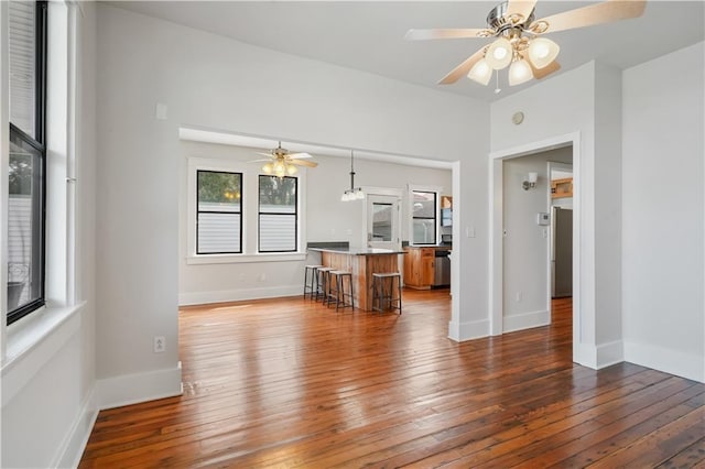 unfurnished living room featuring hardwood / wood-style flooring, baseboards, and ceiling fan