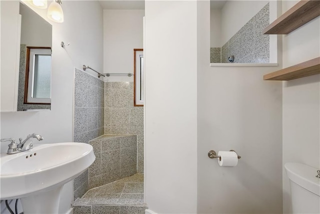 bathroom with a tile shower, toilet, and a sink