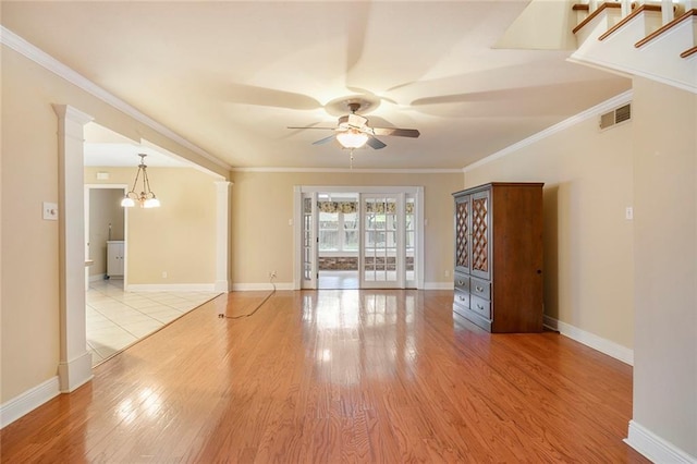 spare room featuring visible vents, ceiling fan with notable chandelier, wood finished floors, and decorative columns