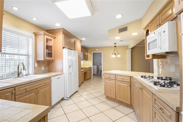 kitchen featuring visible vents, a sink, white appliances, a peninsula, and glass insert cabinets