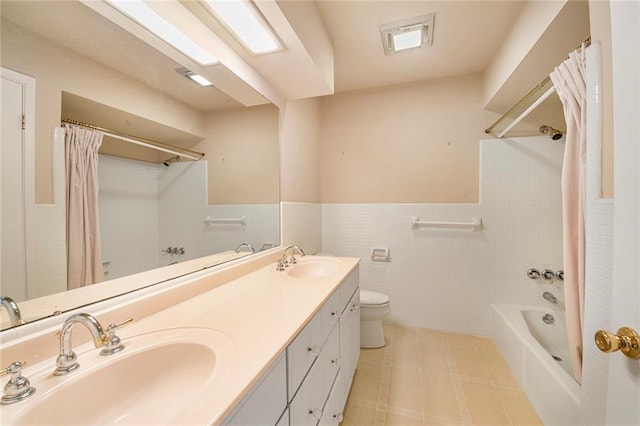 bathroom featuring wainscoting, toilet, tile walls, and a sink