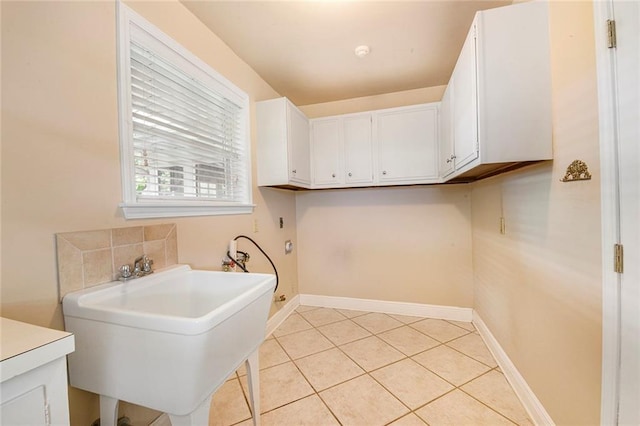 clothes washing area featuring baseboards, light tile patterned floors, hookup for a washing machine, cabinet space, and a sink