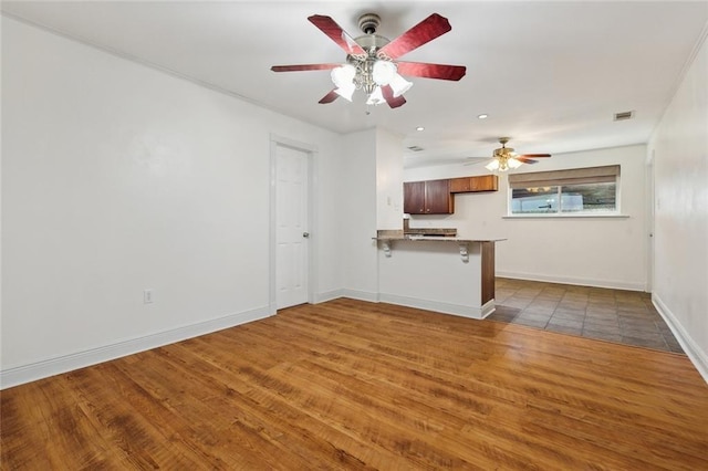 kitchen featuring visible vents, baseboards, a breakfast bar, a peninsula, and wood finished floors