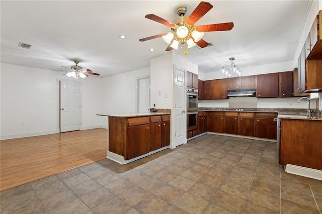 kitchen with a peninsula, a sink, cooktop, under cabinet range hood, and double oven