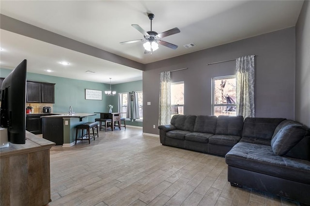 living room featuring visible vents, light wood-style flooring, ceiling fan with notable chandelier, and baseboards