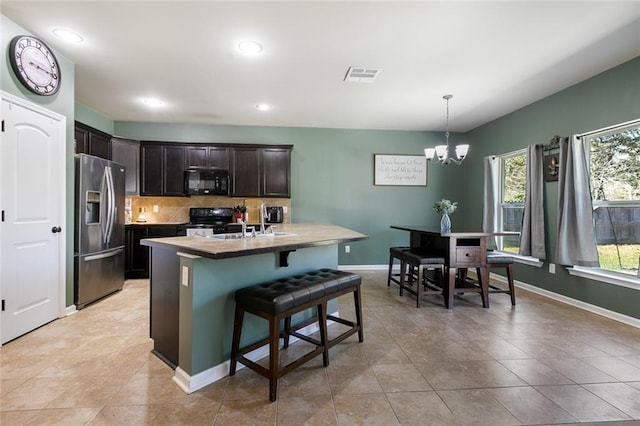 kitchen featuring visible vents, black appliances, a breakfast bar, backsplash, and dark brown cabinets