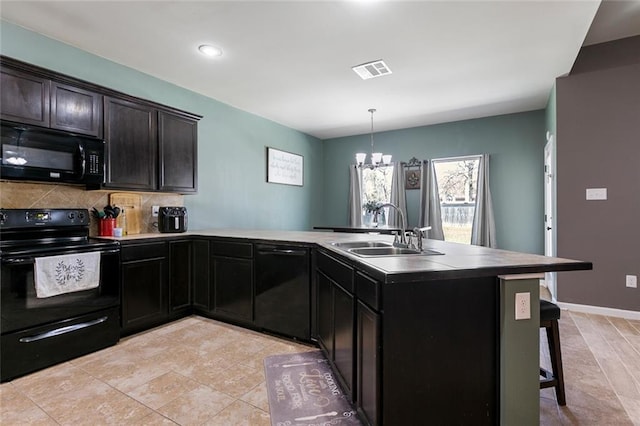 kitchen featuring visible vents, a peninsula, a sink, black appliances, and a kitchen breakfast bar