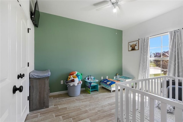 bedroom with wood finish floors, baseboards, a nursery area, and ceiling fan